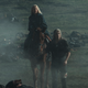 Geralt, on foot, leads Ciri and her horse across a smoky battlefield littered with corpses.